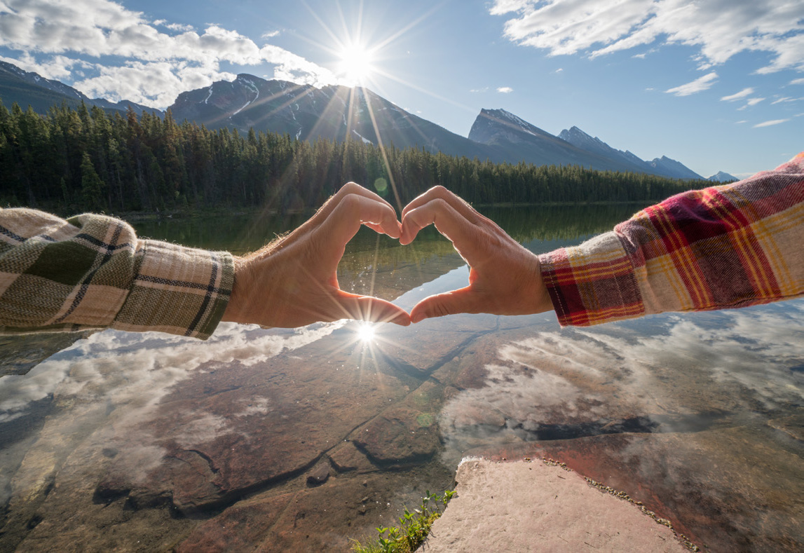 Image of two hands forming a heart over a lake